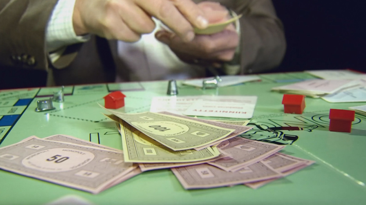 Monopolin pelilauta, henkilö lyö rahaa pöydälle.