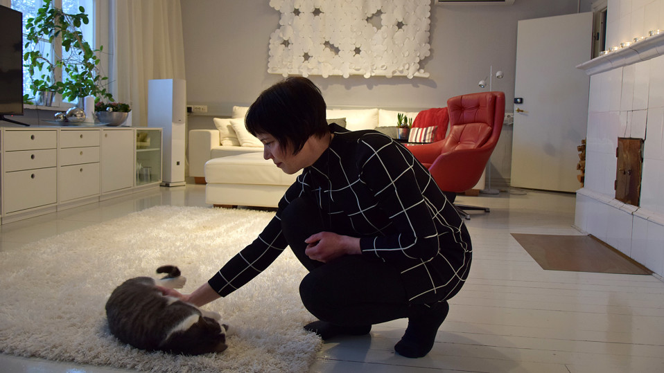Nainen silittää lattialla makaavaa kissaa olohuoneessa
