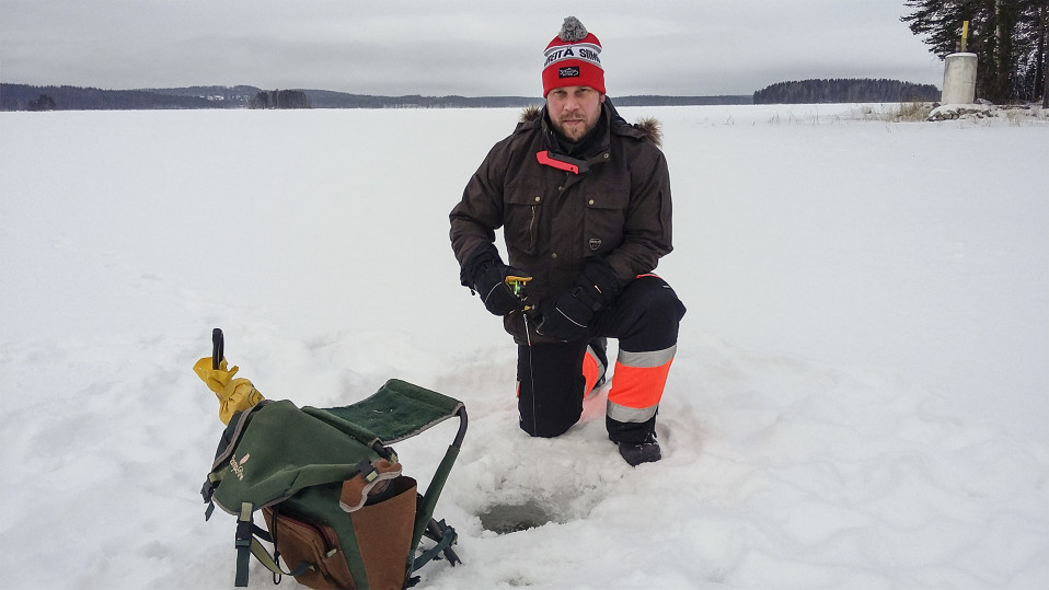 Mies on polvillaan järven jäällä pilkkiavannon edessä.