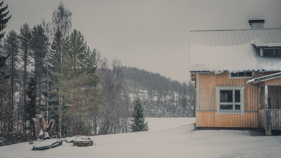 Maatalo talvisessa metsä- ja järvimaisemassa.