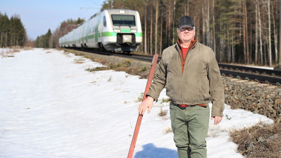 Ossi Hämäläinen seisoo raiteen varrella, kun juna menee selän takaa ohi