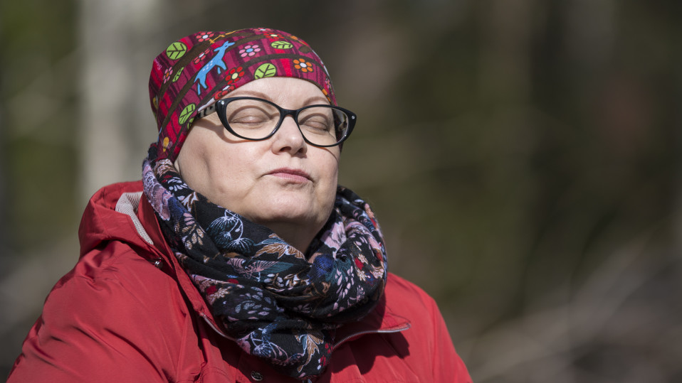 Nainen istuu auringossa silmät kiinni.