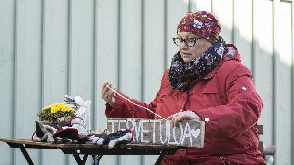 Nainen laittaa ripustusnarua puiseen kylttiin.