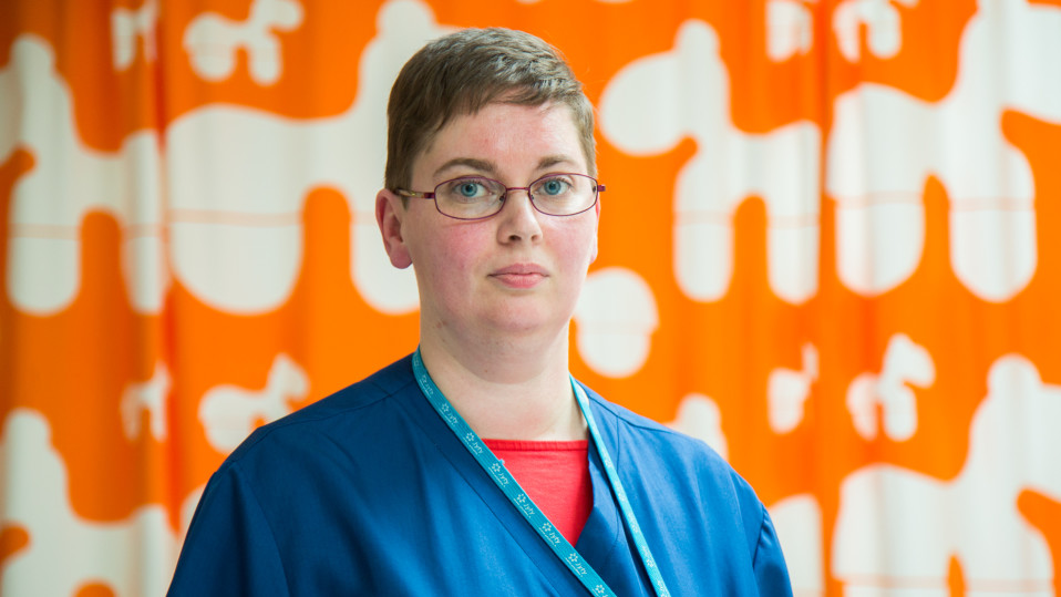 Kajaanilainen Minna Romppainen seisoo oranssin verhon edessä.