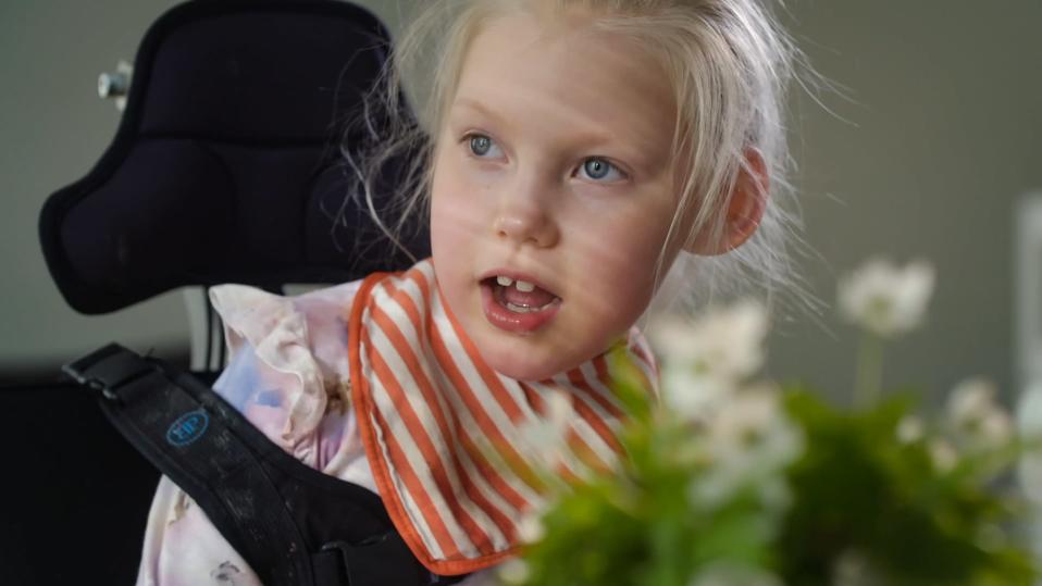 Kehitysvammainen pikkutyttö istuu pöydän ääressä, etualalla valkovuokkoja.