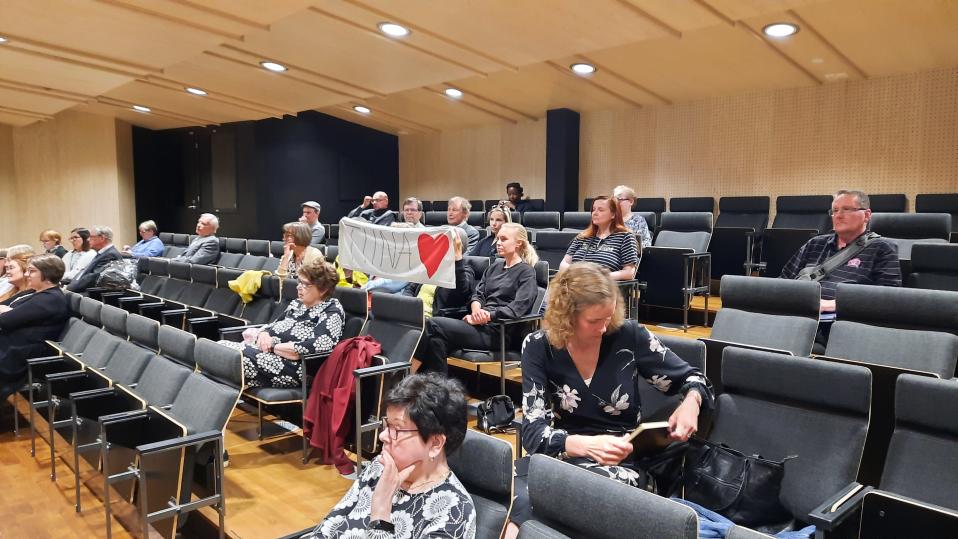 Kokkolan valtuustosalin lehtereillä ihmiset seuraavat valtuuston kokousta, jonka lopuksi päätetään puheenjohtajien erottamisesta. Osalla yleisöstä on puheenjohtajaa tukeva banderolli.