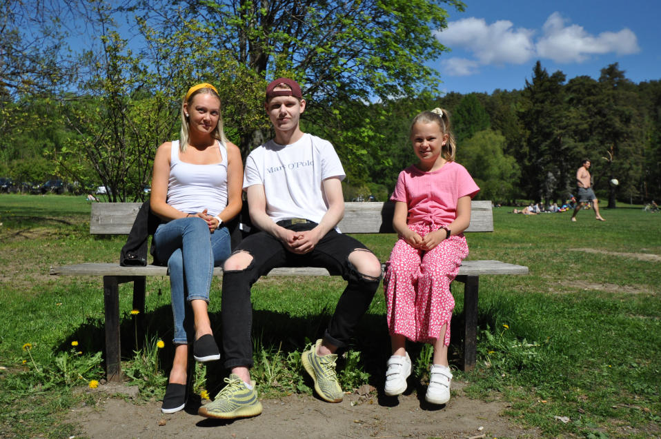 Sisarukset Nella Toiviainen, 17, ja Jemina Toiviainen, 10 istuvat puiston penkillä, välissä lippispäinen Roni Tiikkaja, 17.