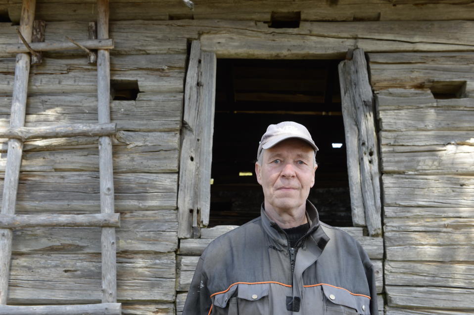 Luomuviljelijä Lauri Takala, jonka taustalla on vanha aittarakennus.