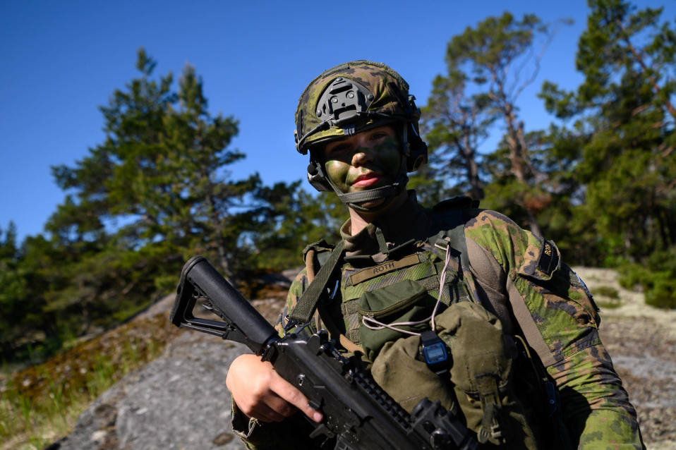 Suomalainen varusmies seisoo kalliolla ja katsoo kameraan hymyillen.