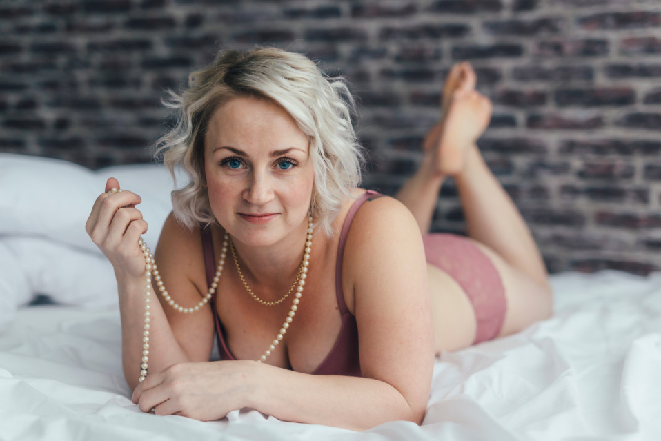 Elina Pynnönen poseeraa boudoir-kuvassa sängyllä vaaleanpunaisissa alusvaatteissa.