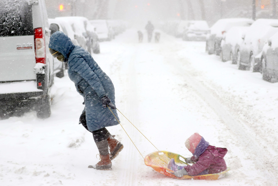 A woman pulls a child on a sled in the middle of a snowstorm in New York.