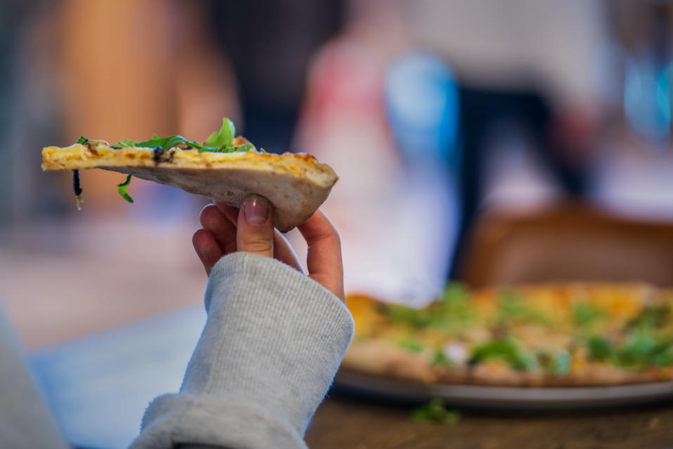 Nuoren tytön käsi pitelemässä pizzapalaa.
