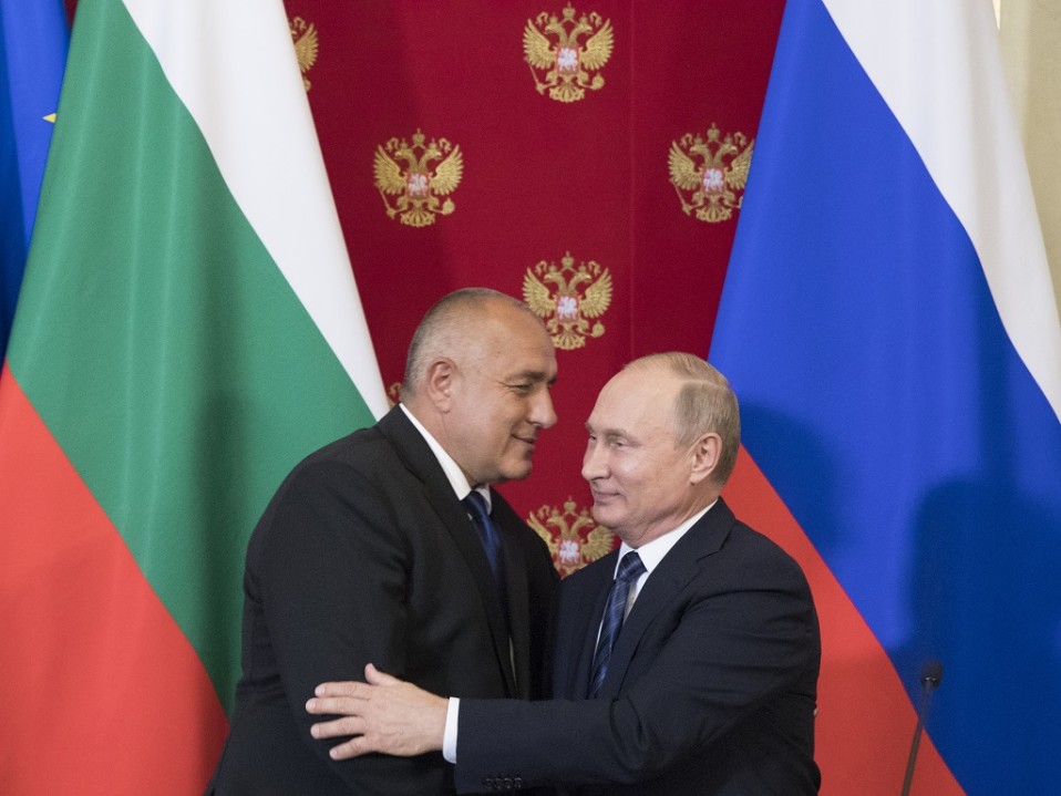 Borisov ja Putin syleilevät. Taustalla ovat Bulgarian ja Venäjän liput ja Venäjän kaksipäistä vaakunakotkaa esittävillä kuvilla koristeltu punainen kangas.
