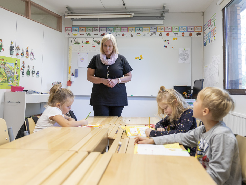 Nainen opettaa kolmea lasta luokassa.