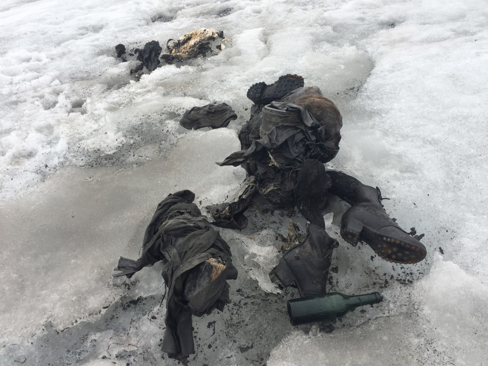 Jäätikön jäässä vanhanaikaiset vaellussaappaat ja lasipullo sekä vanhanaikaisen näköisiä vaatteita.