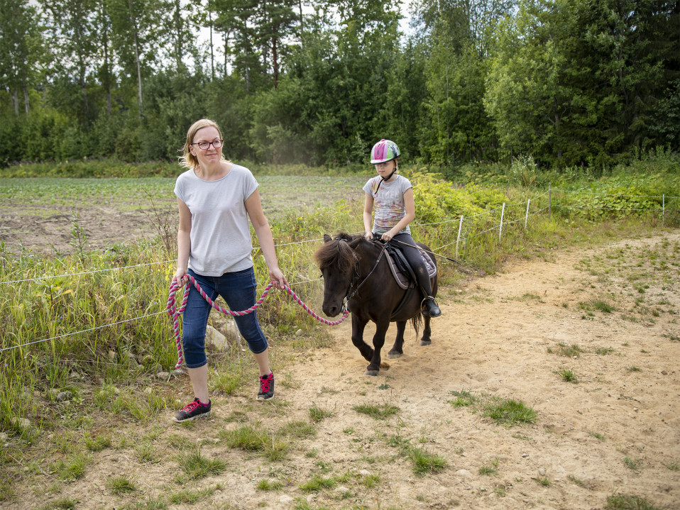 Nainen taluttaa ponia ja pientä ratsastajaa.
