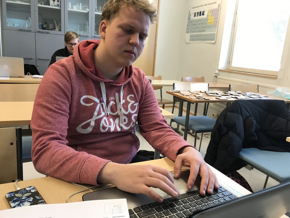 Nuori mies kirjoittaa läppärillä lukion pulpetissa