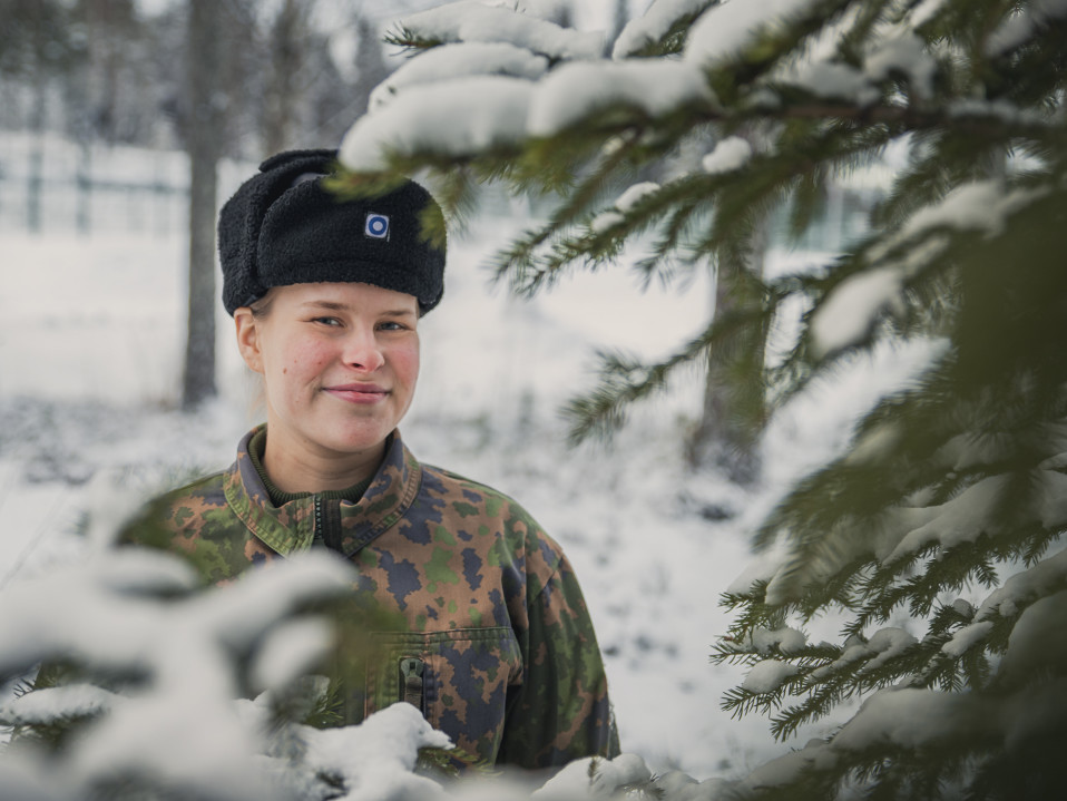 Varusmies hymyilee karvalakki päässä ulkona.