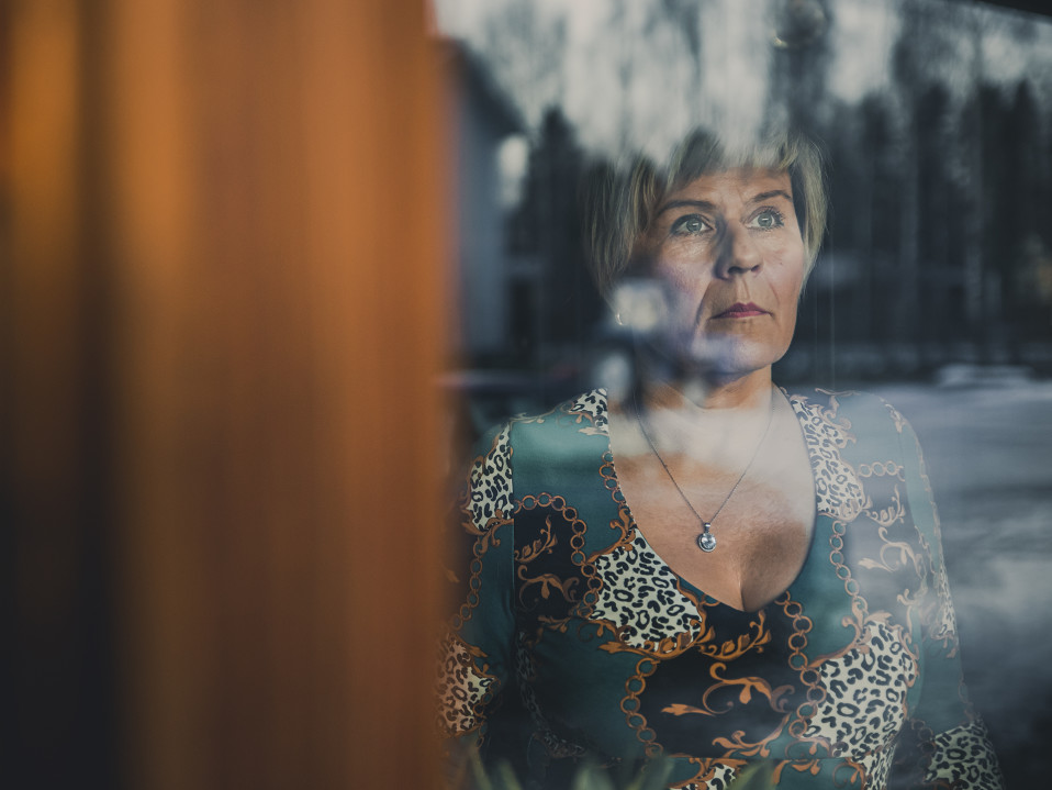 Päivi Varakas katselee ulos kotinsa ikkunasta vakava ilme kasvoillaan.