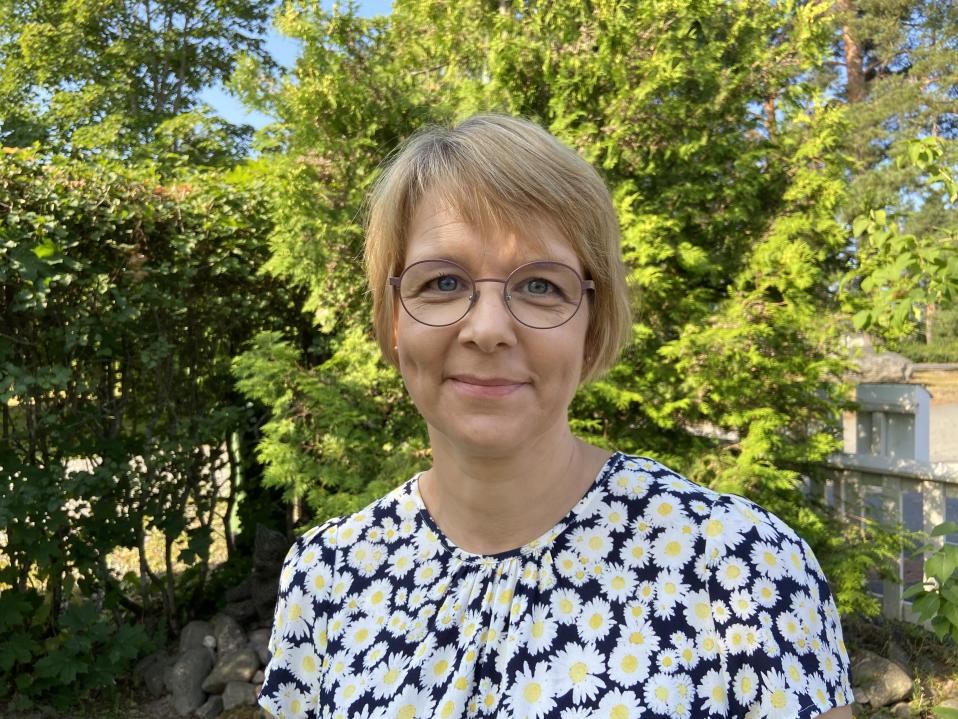 Kirsi Flinck seisoo kotipihallaan. Takana näkyy tuija, jossa mehiläisparvi majaili.