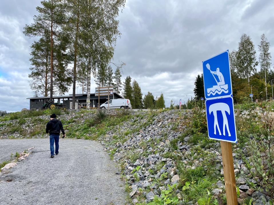 Melontaopaste Iitin Vuolenkoskella, Rantamestan rannassa. Mies kävelee rannasta kohti taustalla kohavaa rakennusta.