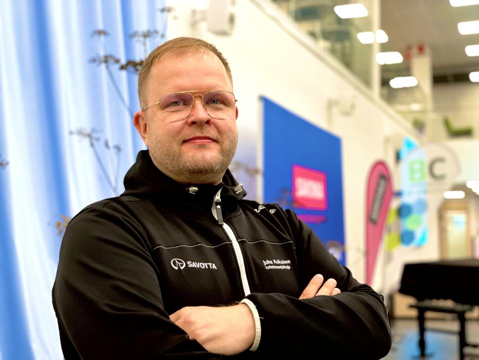 Juha Asikainen seisoo kädet puuskassa oppilaitoksen aulatilassa.