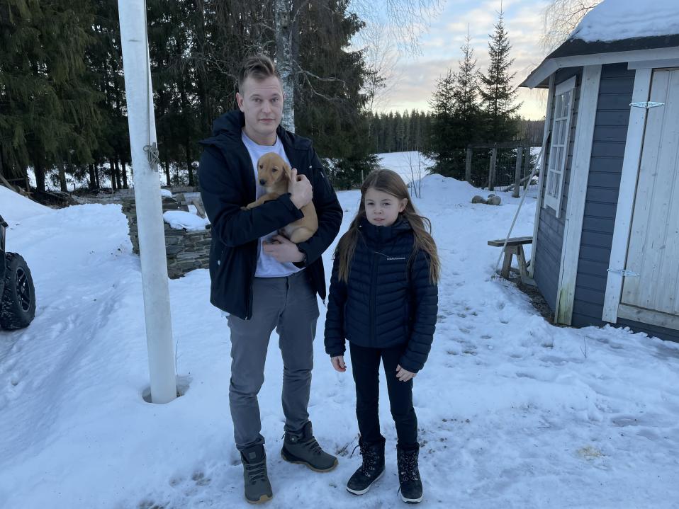 Mies seisoo talvisessa maisemassa koiranpentu sylissä.