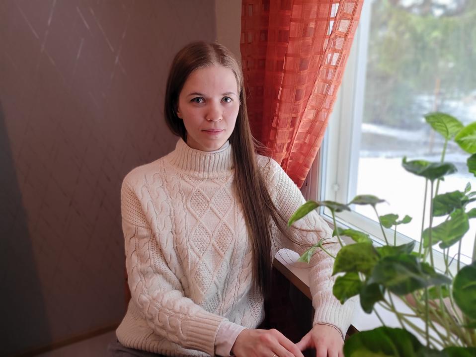 Olga Nakonechna istuu ikkunan vieressä. Hymyilee ja katsoo kameraan.
