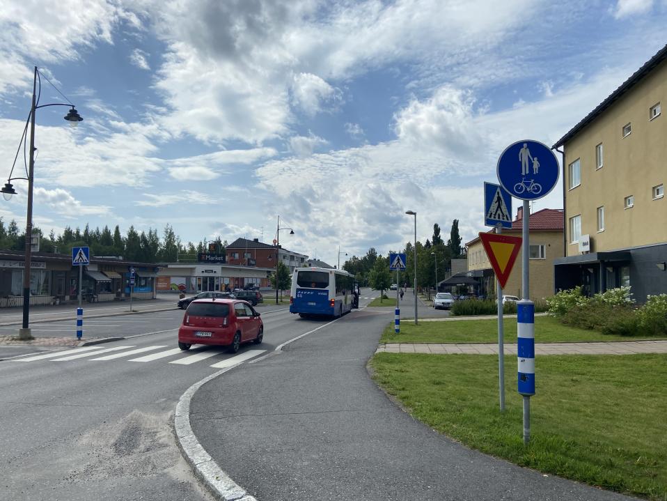 Kuhmoisten keskustan keskusraitti. Tampereen liikenteen Nysse on pysähtyneenä ottamaan ja sen perässä on punainen pikkuauto