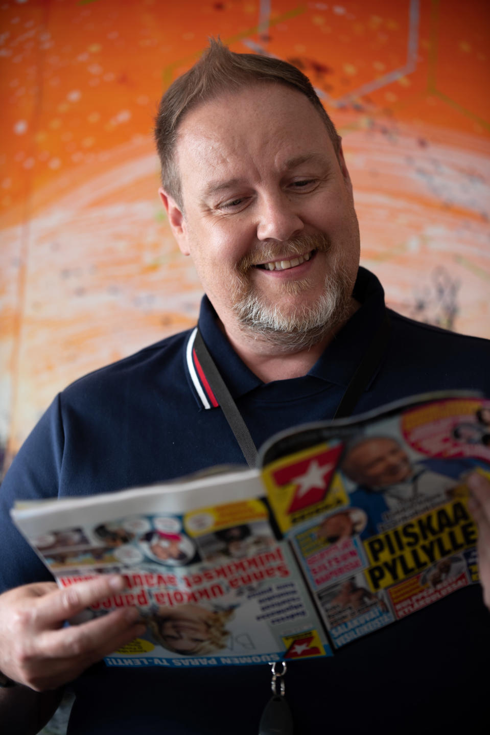 Jari Peltomäki lukee Seiskaa oranssin taustan edessä.