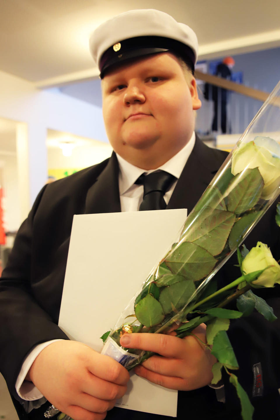 Teemu Kiviniemi valkolakki päässä, ruusut ja tutkintotodistus kädessään.