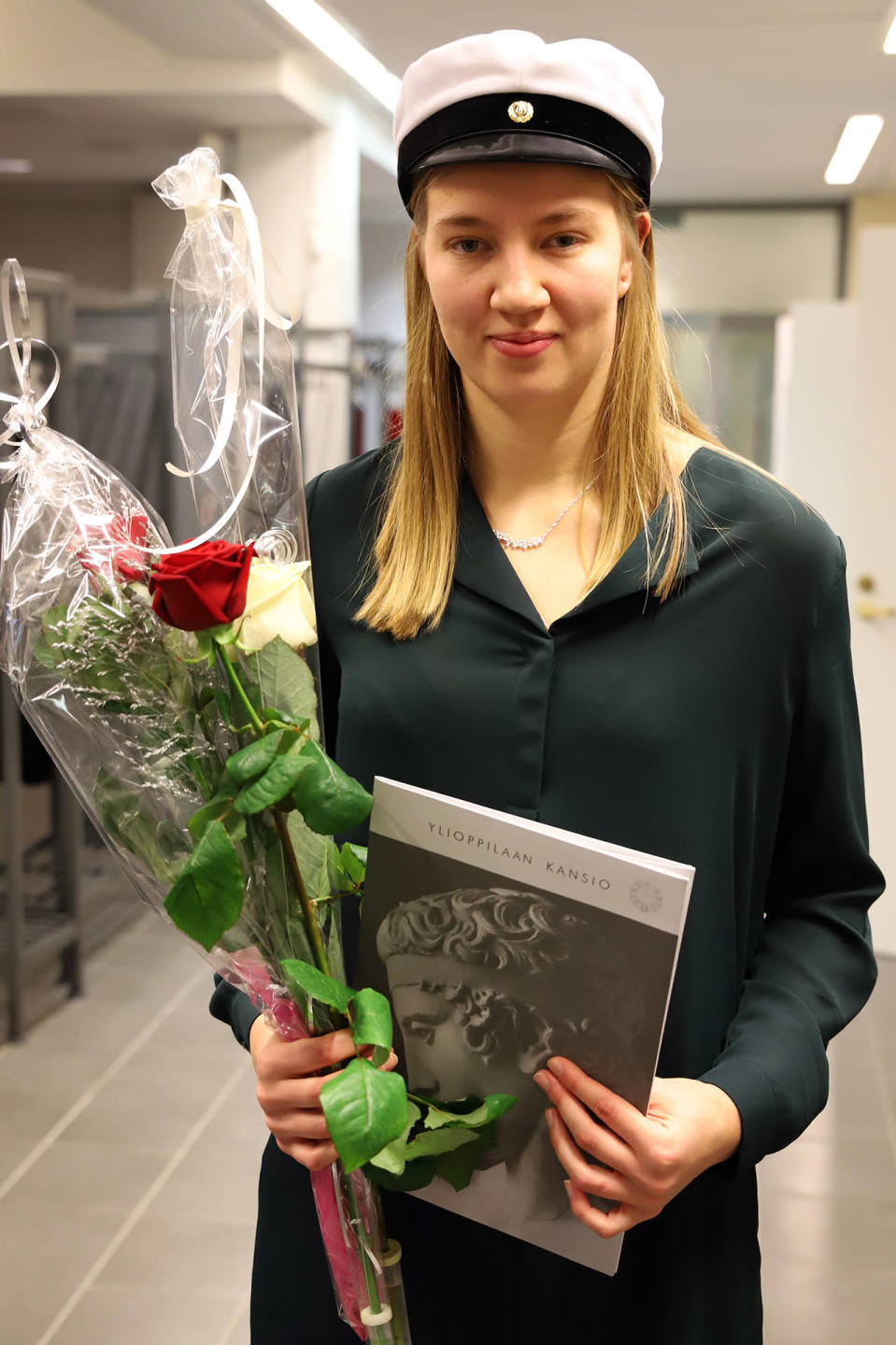 Mette Baas valkolakki päässään, kukat ja ylioppilastutkintotodistus kädessään.