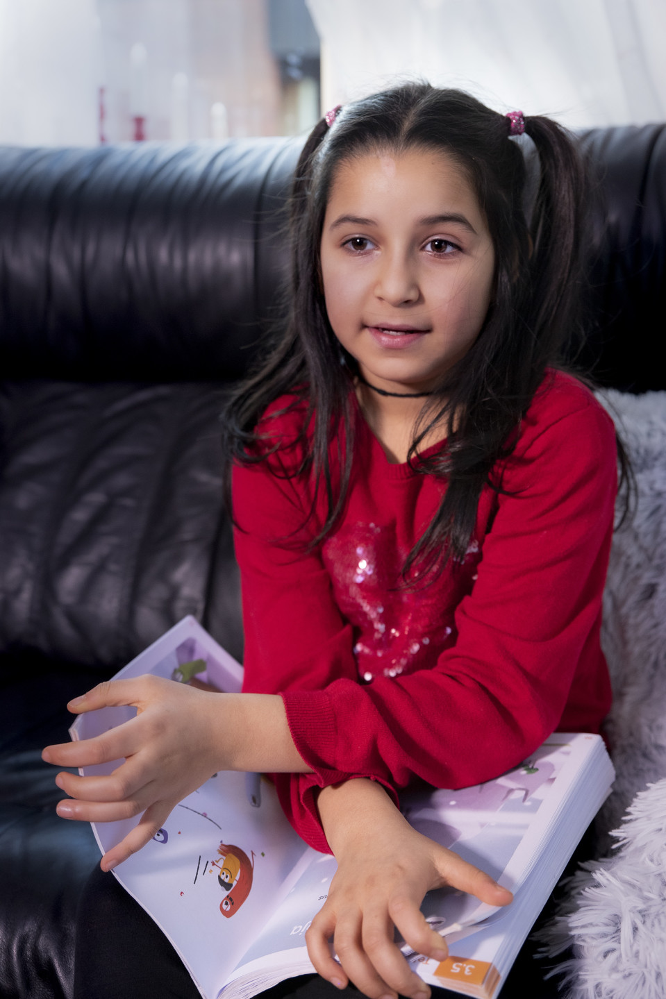Husna Azimi istuu kotona sohvalla koulukirja kädessä.
