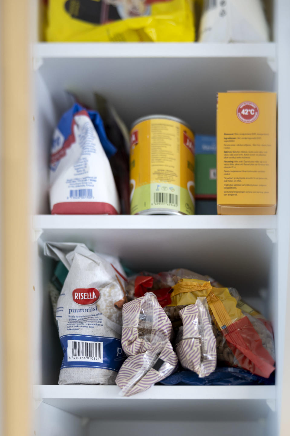 Riisiä, spagettia, makaronia, sokeria, hernekeittoa ja muita ruoka-ainepakkauksia kaapissa.