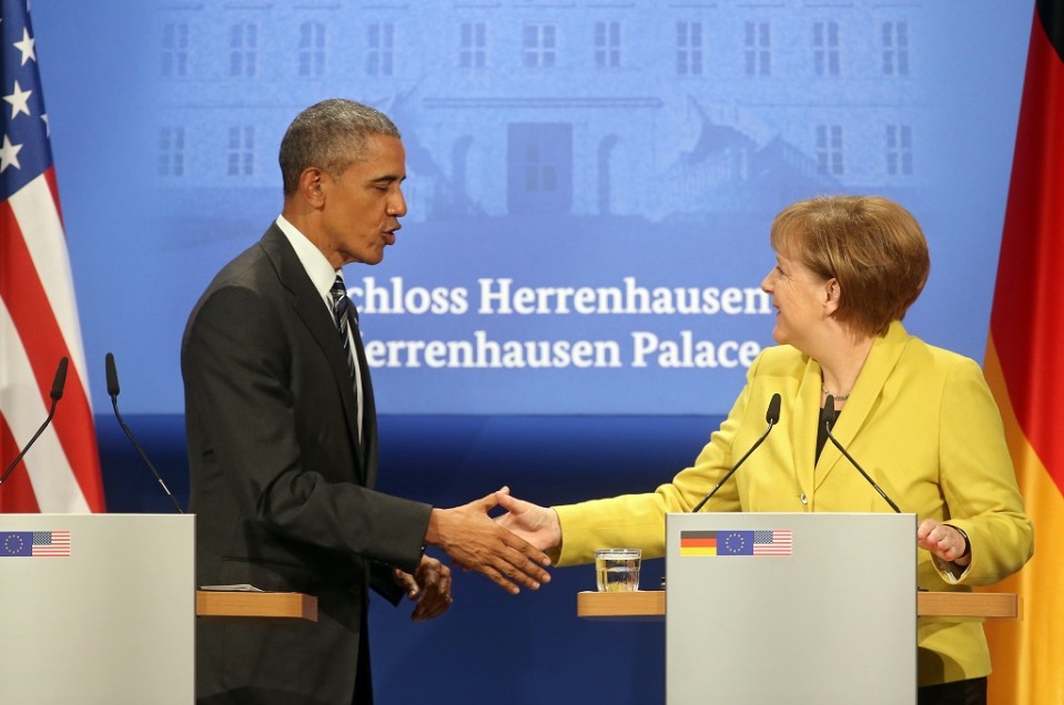 Puhujakorokkeella seisovat Obama ja Merkel kättelevät. Taustalle on heijastettu Herrenhausenin linnan julkisivun kuva.