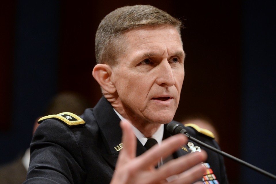 Flynn puhuu mikrofoniin vahvistaen sanojaan oikealla kädellään. Hänellä on yllään tumma univormu, jonka kauluksessa on kultaisin kirjaimin U.S. Rintamuksessa on sarja ansiomerkkejä. Kuvan tausta on musta.