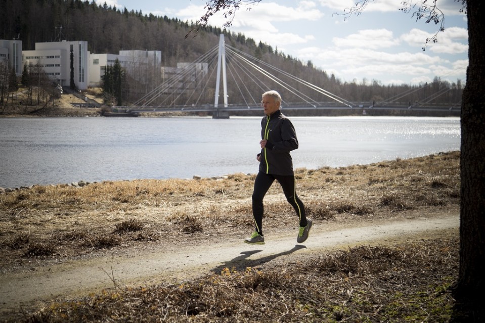Veryttelypukuinen Issakainen juoksee rantapolulla Jyväskylässä. Taustalla Mattilanniemen kävelysilta.