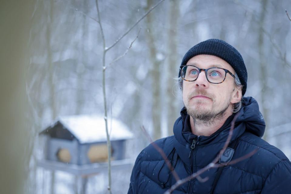 Heikki Helle katsoo taivaalle talvisessa maisemassa. Taustalla lintulauta.