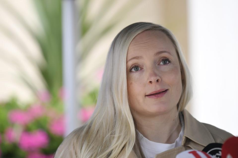 Maria Ohisalo, en blond kvinna klädd i beige kappa, stpr framför en blommande buske.