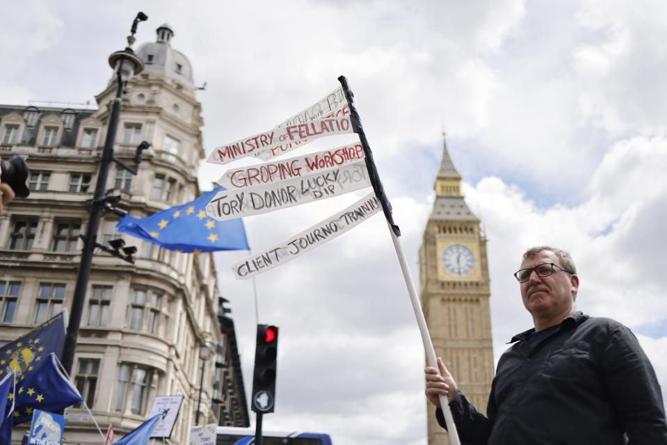 Mielenosoittaja seisoo Britannian parlamentin edessä kädessään kyltti, jossa on tienviittoja.