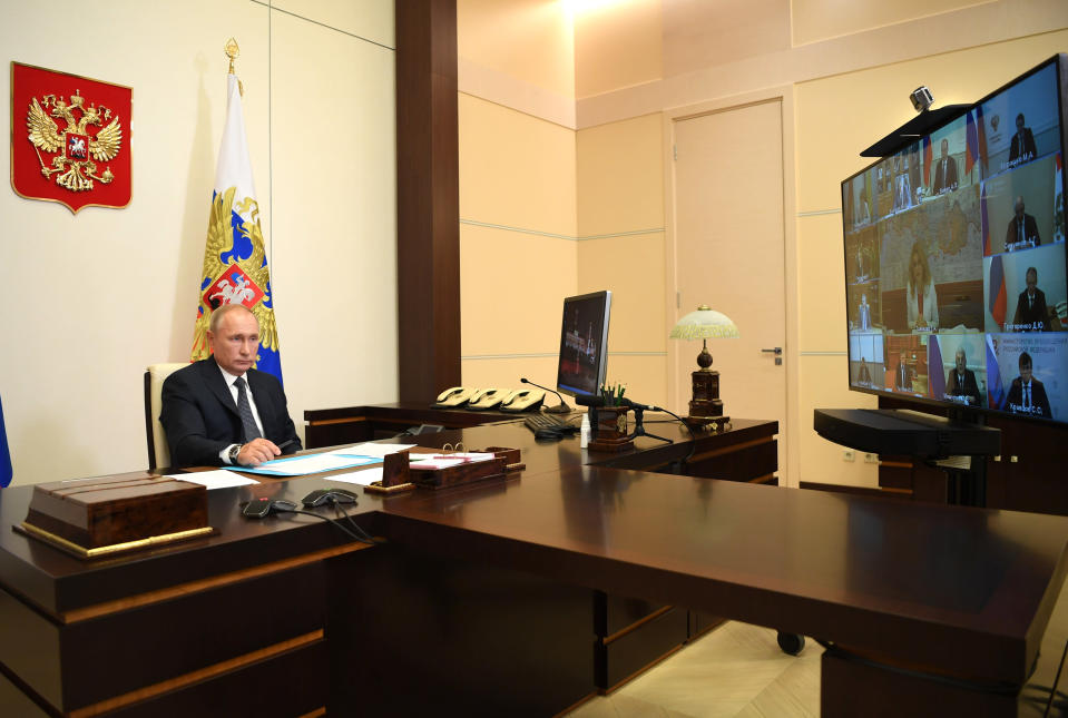 Vladimir Putin istuu toimistossa pöydän takana, edessä suurella videoruudulla Venäjän hallituksen ministereitä