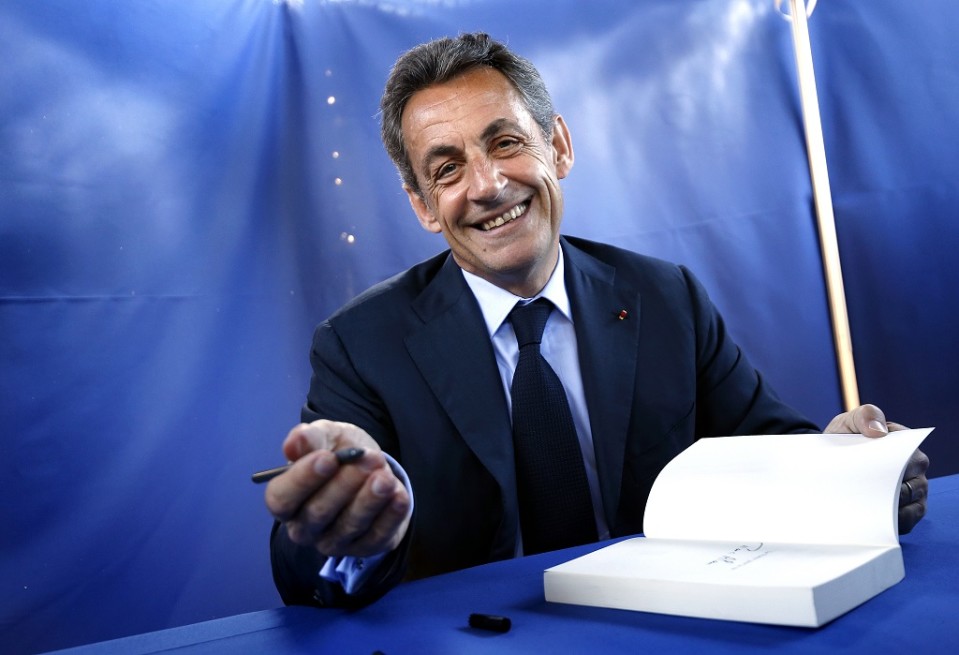 Nicolas Sarkozy katsoo kameraan ja virnistää.