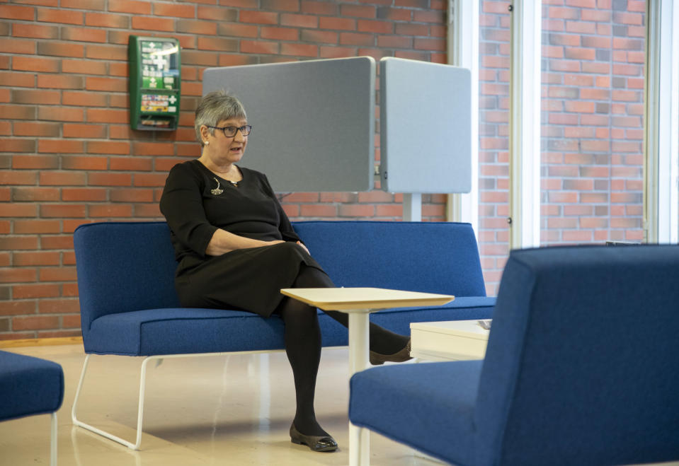 Annikki Niiranen istuu aulan sinisellä sohvalla, taustalla on tiiliseinä