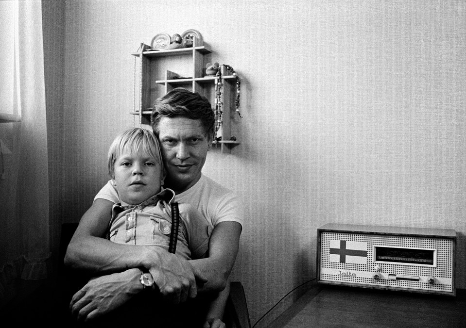 Poika istuu isän sylissä. Radio, radiovastaanotin, jossa on Suomen lippu.