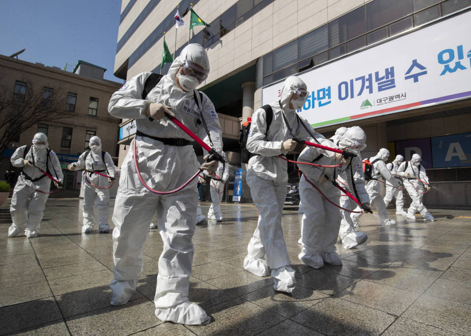 Suoja-asuihin pukeutuneet sotilaat suihkuttavat desinfiointinestettä kadulle Daegussa Etelä-Koreassa 2. maaliskuuta 2020.