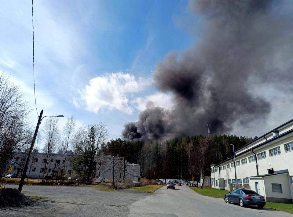 Röken från en stor brand i en pappersmaskinfabrik stiger upp bakom skogsdunge i Jyväskylä.