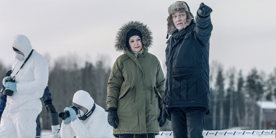 Sorjonen (Ville Virtanen) osoittaa sormella kuvan ulkopuolelle. Lena Jaakkola (Anu Sinisalo) katsoo sormen osoittamaan suuntaan, taustalla rikospaikkatutkijoita valkoisissa puvuissaan.