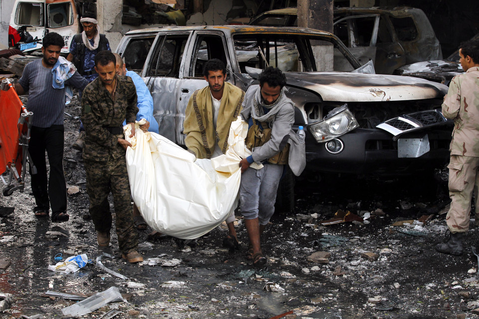 Yemeniläisiä miehiä kantamassa kuollutta henkilöä ulos raunioista.