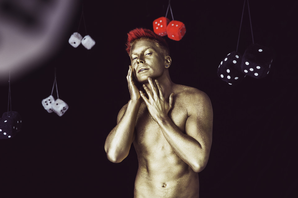 Antti Tuisku kullatussa kropassa ja punaisilla hiuksilla poseeraa mustalla taustalla Kesäkumibiisin videolla. Antin ympärillä on karvanoppia.