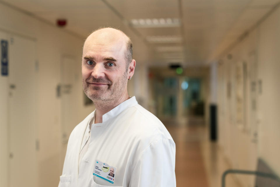 Perinnöllisyyslääkäri Kirmo Wartiovaara hymyilee valkeassa takissaan naistenklinikan käytävällä.